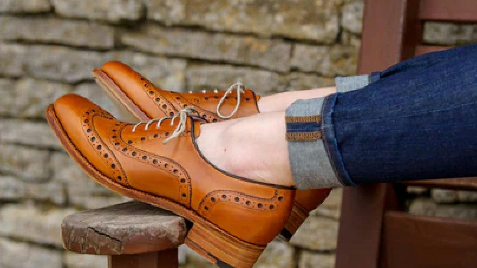 Crossed feet in tan leather brogues with light laces, worn with cuffed blue jeans (photo: Dhruv Kumar / Unsplash)