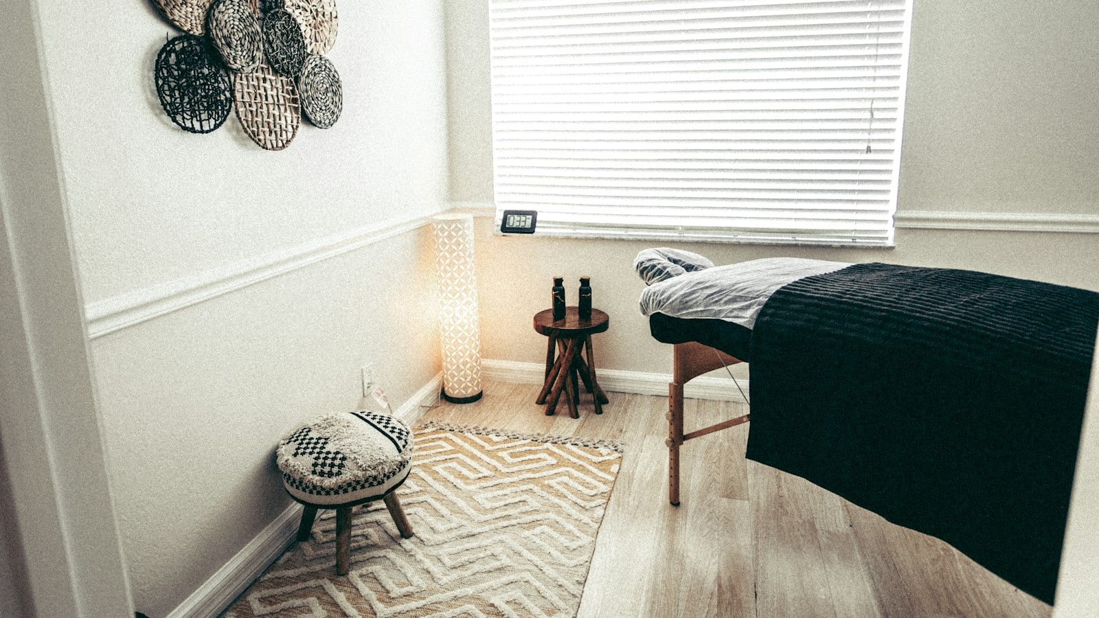A calm treatment room with a massage table, woven rug, floor lamp and woven wall decorations (photo: Cherosi / Unsplash)