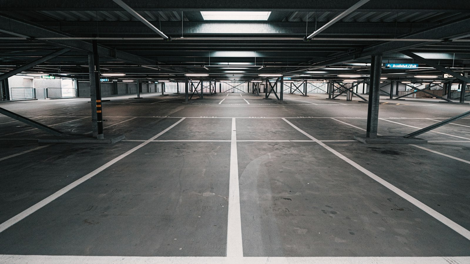An empty, brightly lit parking garage level with white lane markings running into the distance (photo: Claudio Schwarz / Unsplash)
