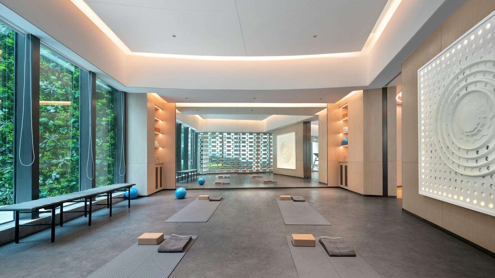 A modern studio with floor-to-ceiling windows, a green wall outside and mats laid out on a grey floor (photo: eran design / Unsplash)
