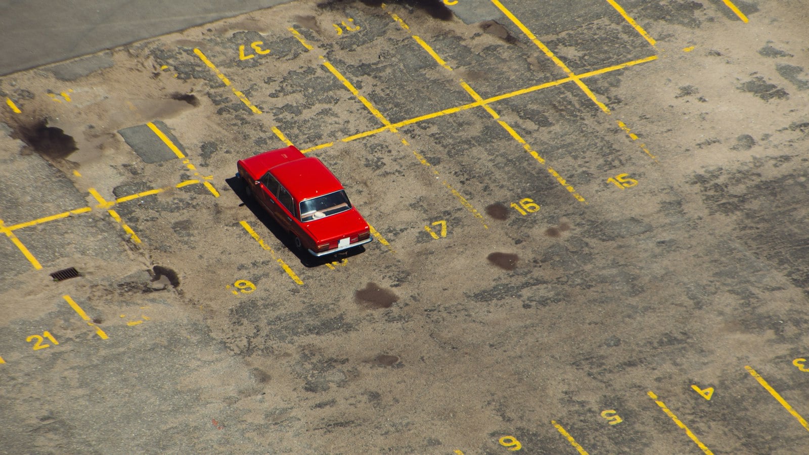 Aerial view of a single red car parked in a numbered bay in an otherwise empty lot (photo: Krzysztof Kotkowicz / Unsplash)