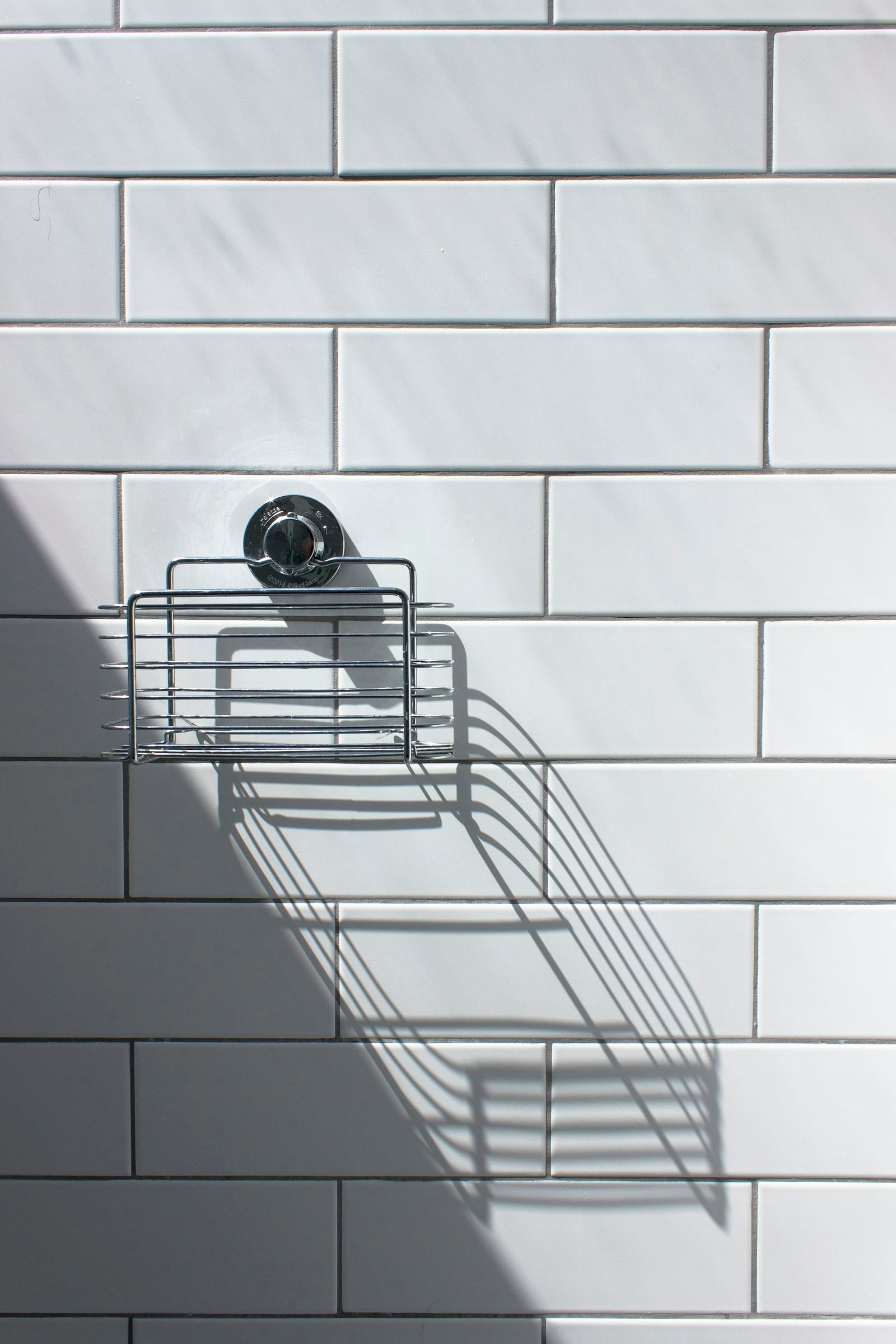 White bathroom tiles with a small wire shelf (photo: Darren Richardson / Unsplash)