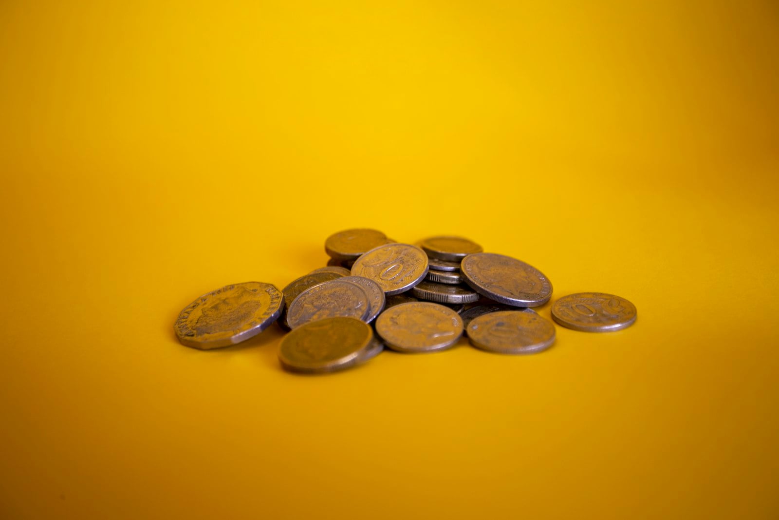 Small pile of coins on a yellow background (photo: Miles Burke / Unsplash)