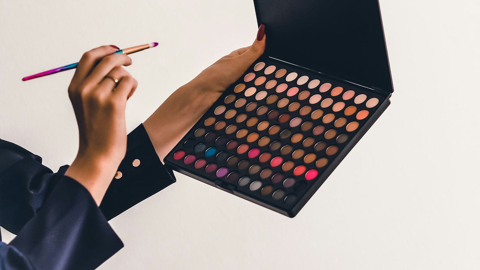 A hand holding an eyeshadow palette and a brush (photo: Laura Chouette / Unsplash)