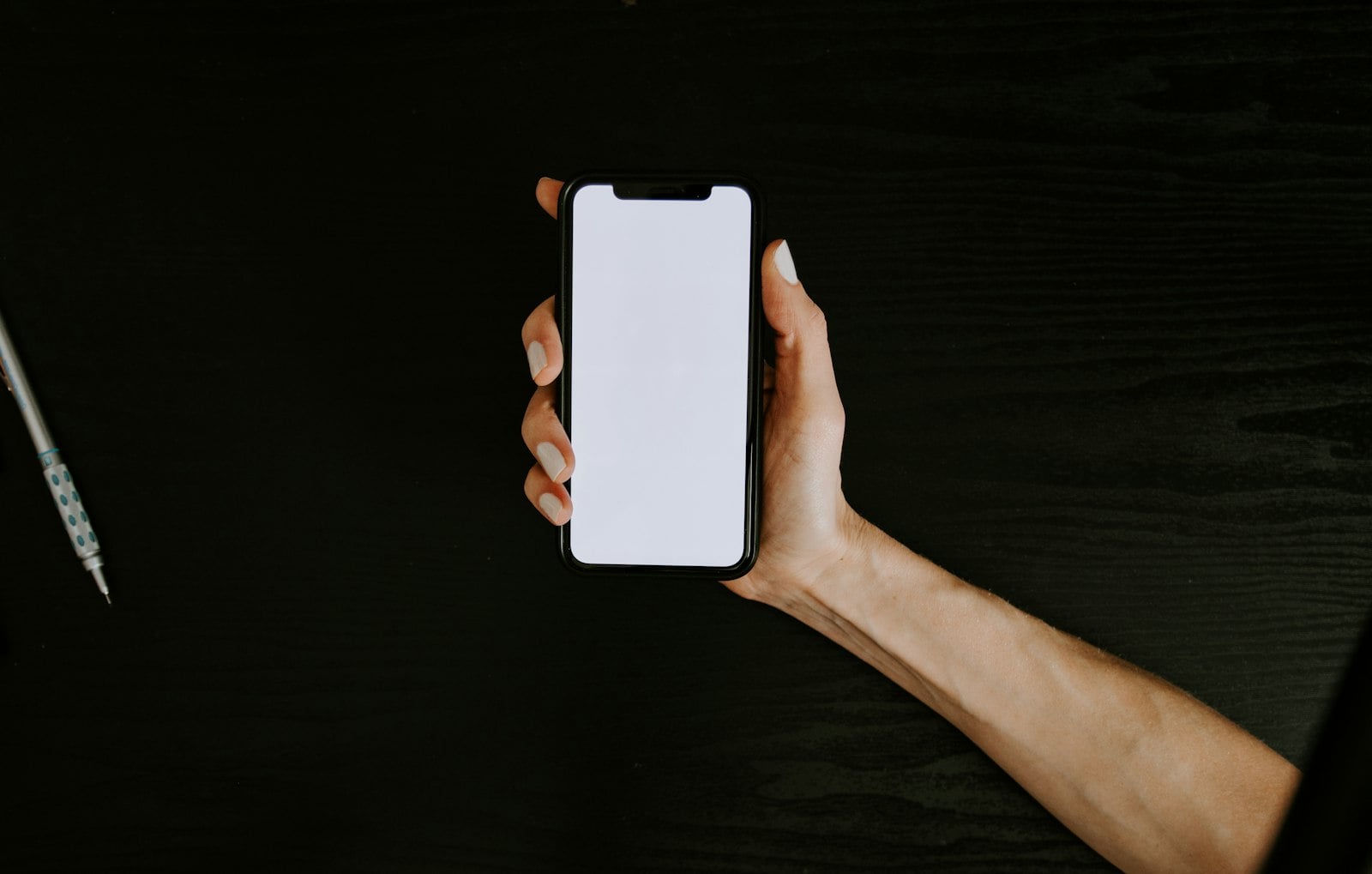 Hand holding a smartphone against a dark background (photo: Kelly Sikkema / Unsplash)