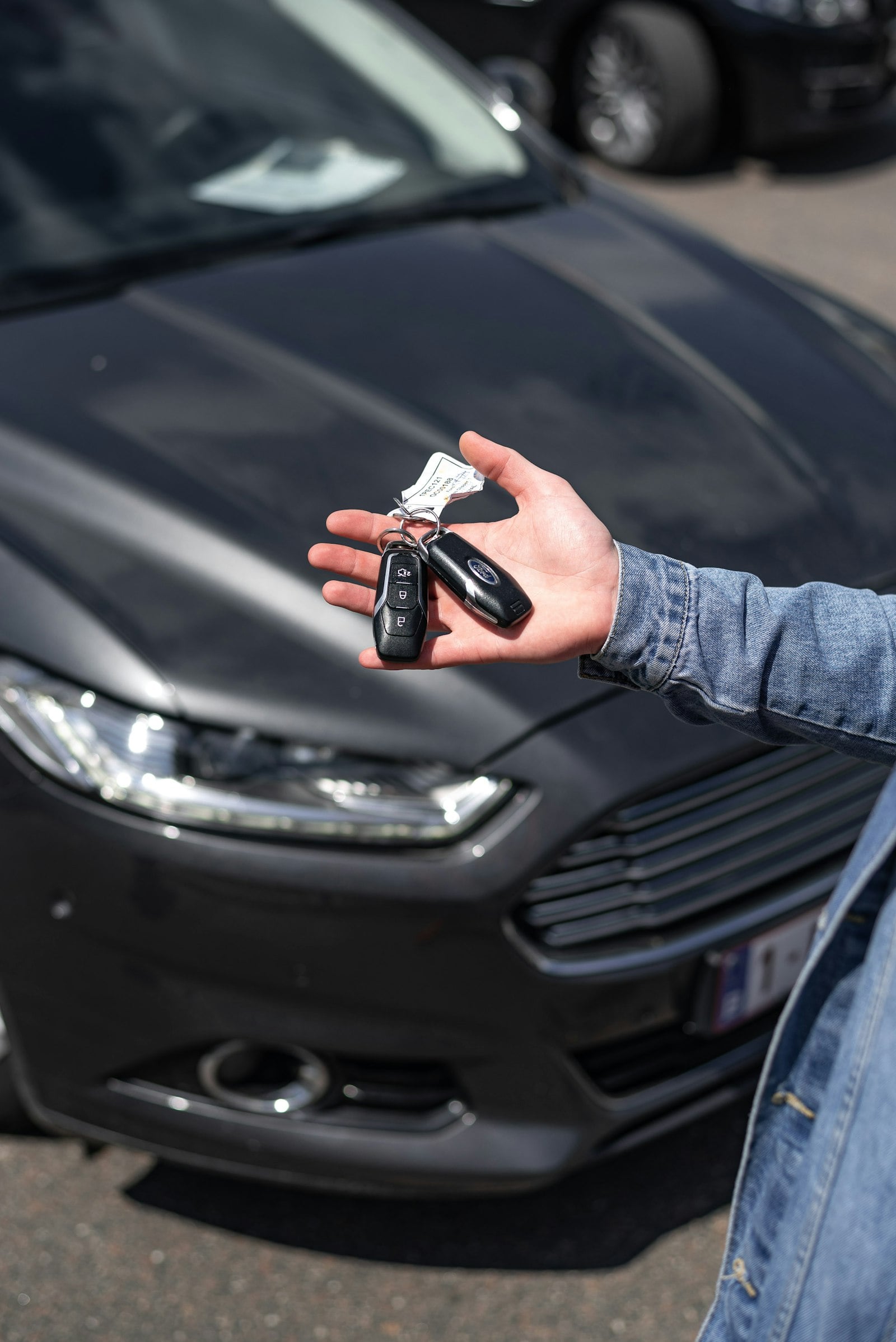 Person holding car keys beside a grey car (photo: Ivan Kazlouskij / Unsplash)