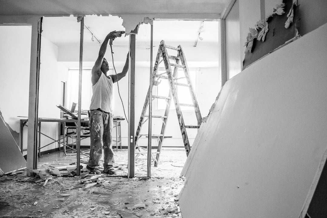 A worker tears out drywall between metal studs in a gutted room with a stepladder nearby