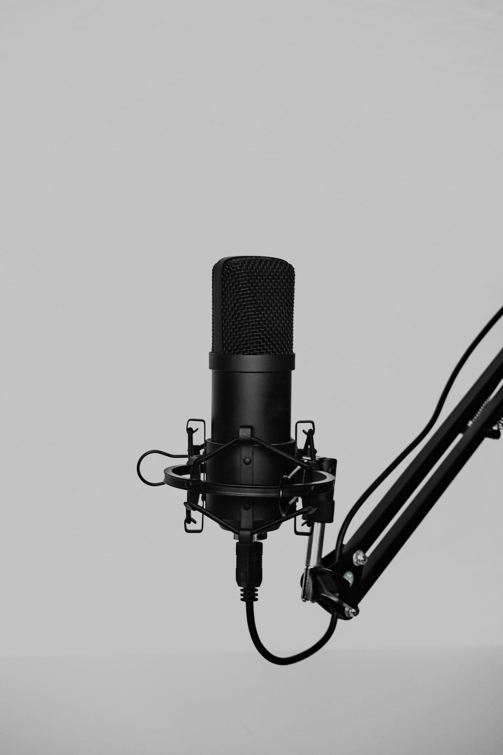 Microphone on a desk arm against a grey wall (photo: Klim Musalimov / Unsplash)