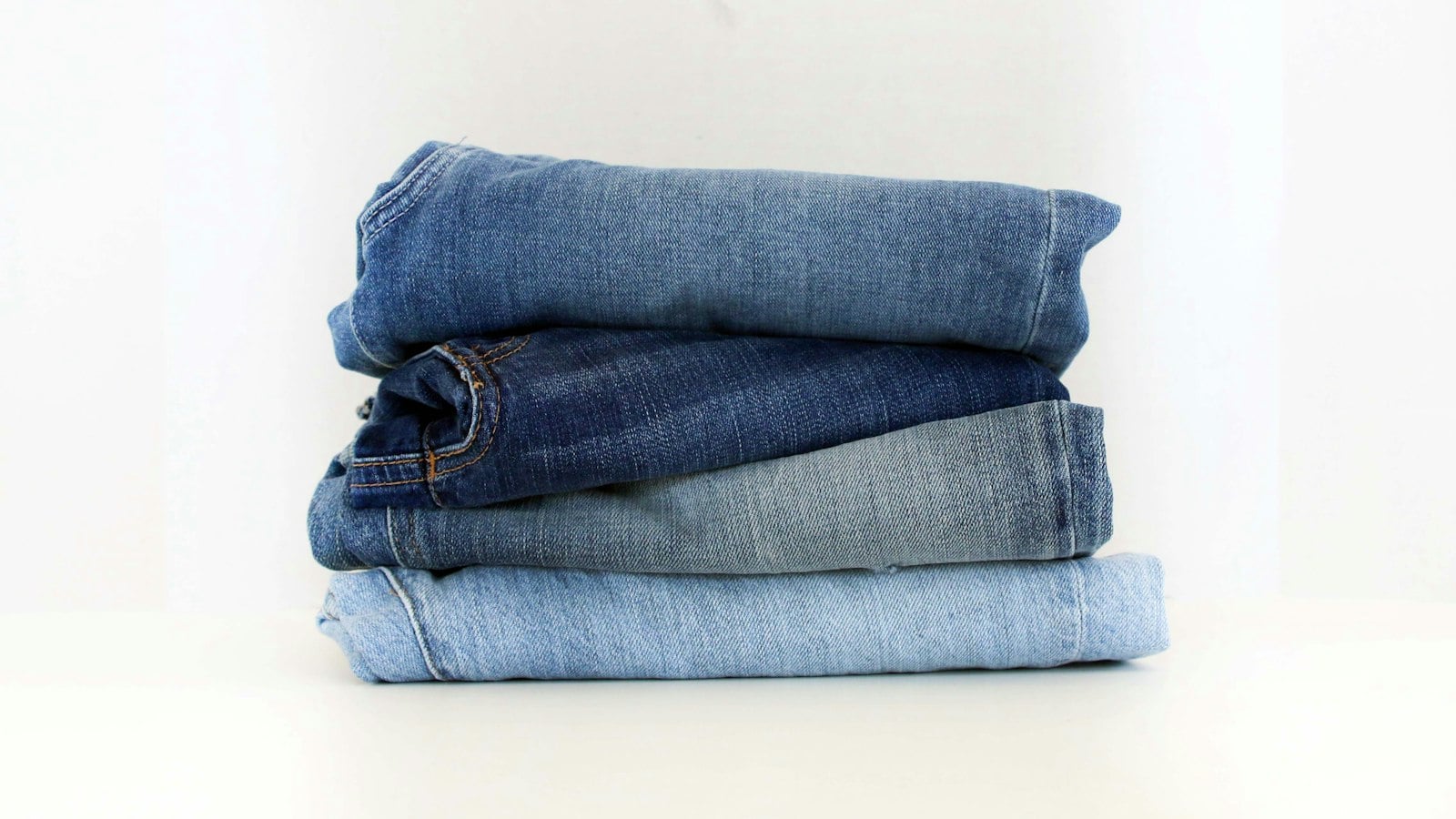 A stack of folded blue jeans on a white background (photo: Claire Abdo / Unsplash)