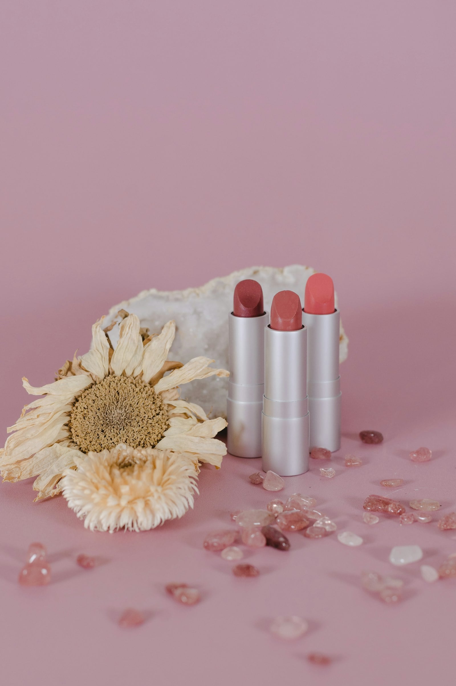 Three pink lipsticks beside a dried flower (photo: Jen Vazquez / Unsplash)