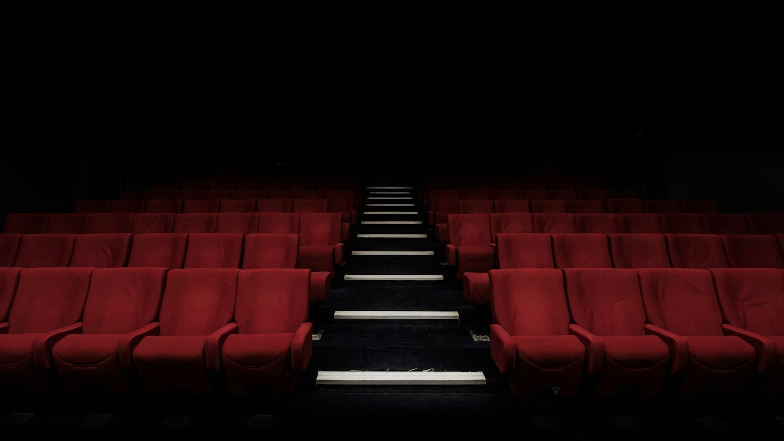 Rows of empty red theatre seats either side of a lit aisle (photo: Felix Mooneeram / Unsplash)