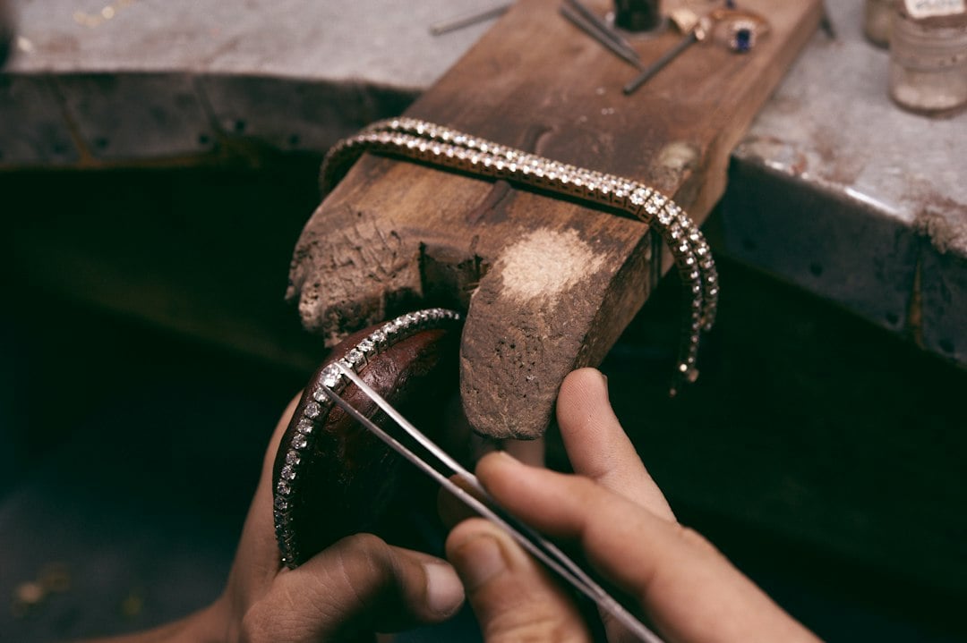 A jeweller's hands working a rhinestone-set bangle over a wooden bench pin.