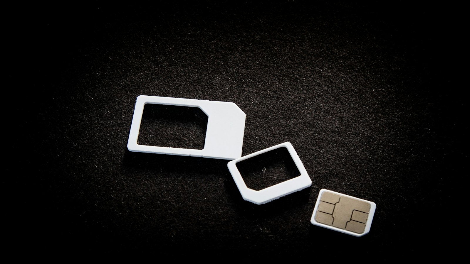 Plain white SIM cards and their adapters laid out on a dark surface (photo: User_Pascal / Unsplash)