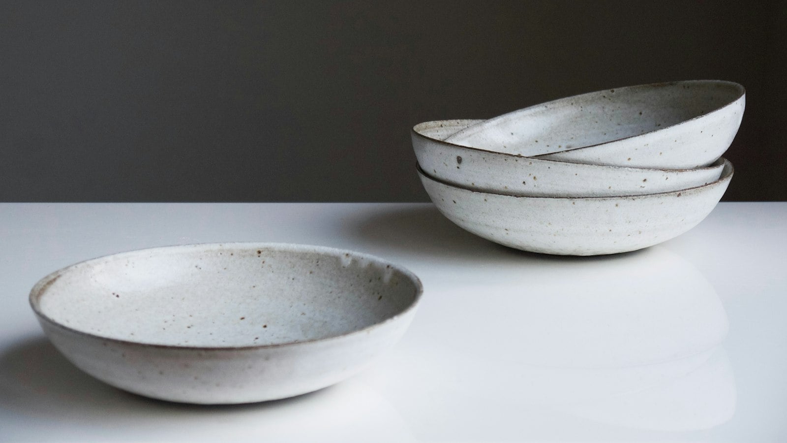 Three speckled, hand-glazed stoneware bowls on a white surface against a dark wall (photo: Tom Crew / Unsplash)