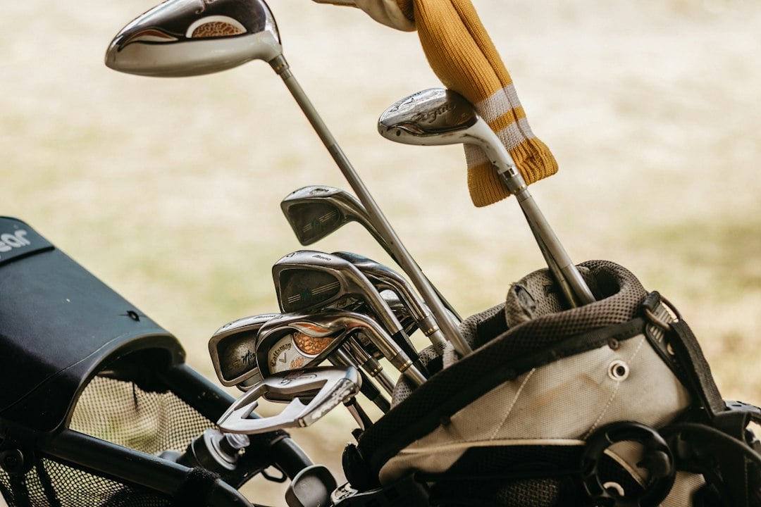 A golf bag filled with irons and drivers, one club wearing a yellow knit headcover
